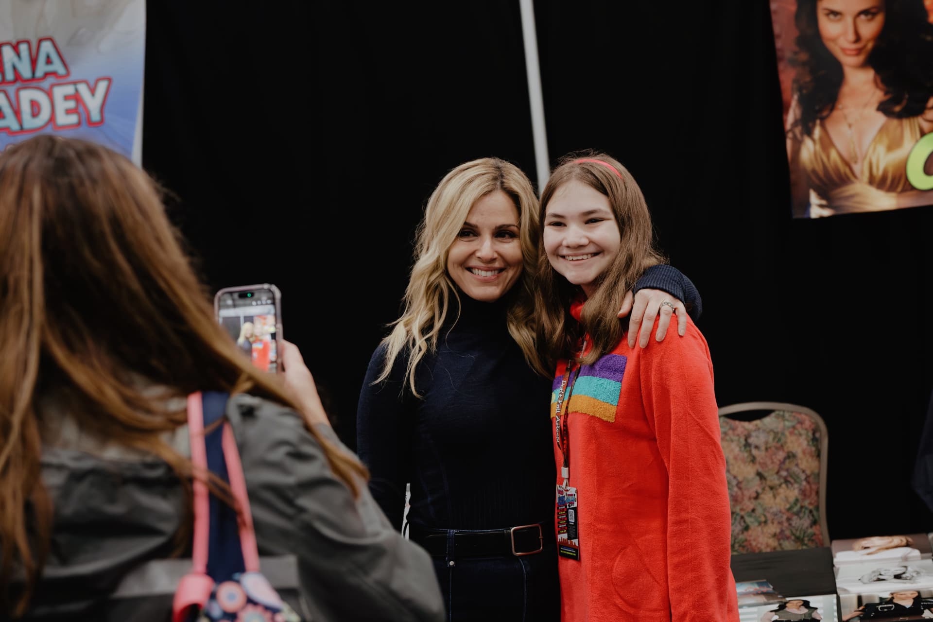 A guest posing with a young fan while a parent takes a photo